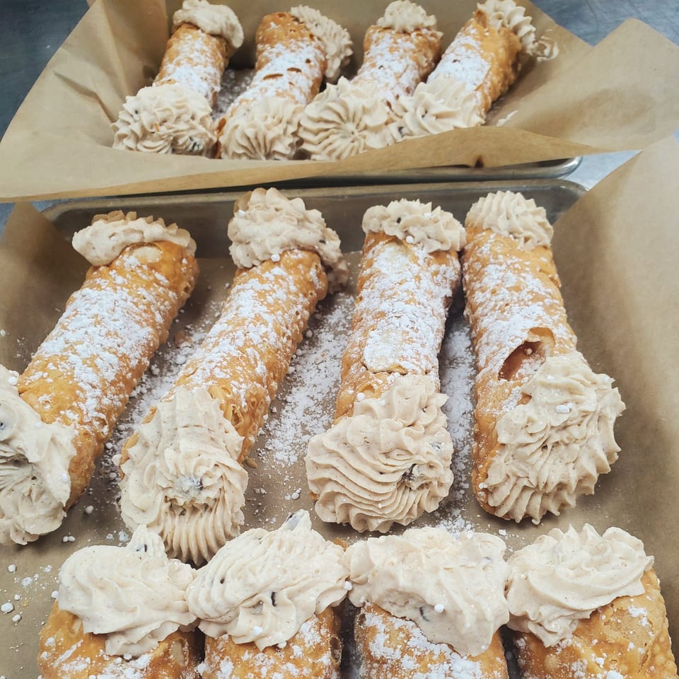 Rows of cannolis with powdered sugar and cream filling on brown parchment paper.