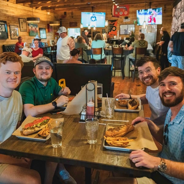 Four men smiling at the camera, enjoying cheesesteaks and fries at Inky's restaurant.