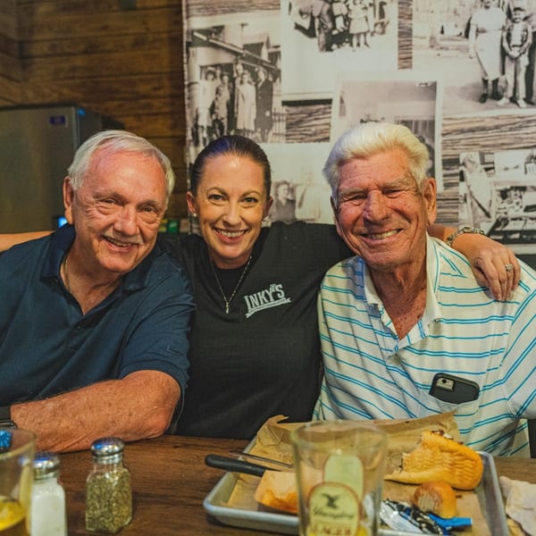 Two smiling older men and a woman in an Inky's shirt pose happily at a table.