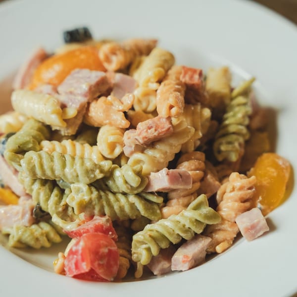Colorful pasta salad with rotini, ham, tomatoes, and bell peppers in a creamy dressing.