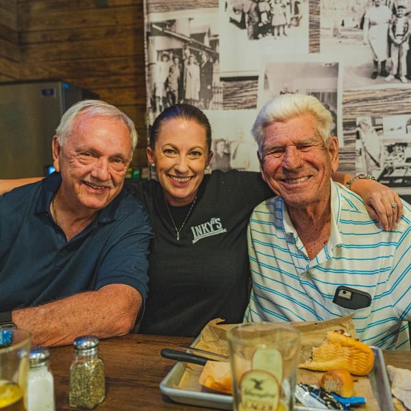 Three smiling people, two men and one woman in an Inky's shirt, sitting at a table.