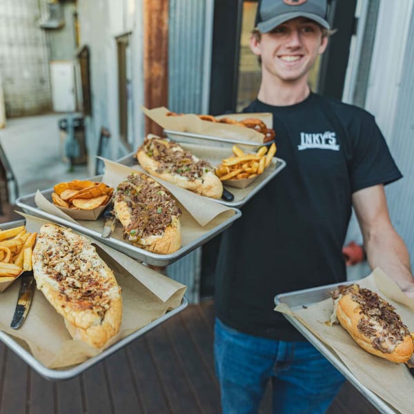 Smiling Inky's employee carrying multiple trays of cheesesteaks, fries, and onion rings.