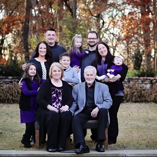 A large family, including children and grandparents, poses outdoors in front of autumn trees.