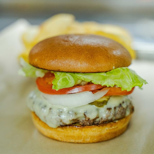 A cheeseburger with melted white cheese, lettuce, tomato, onion, and pickles on a bun.
