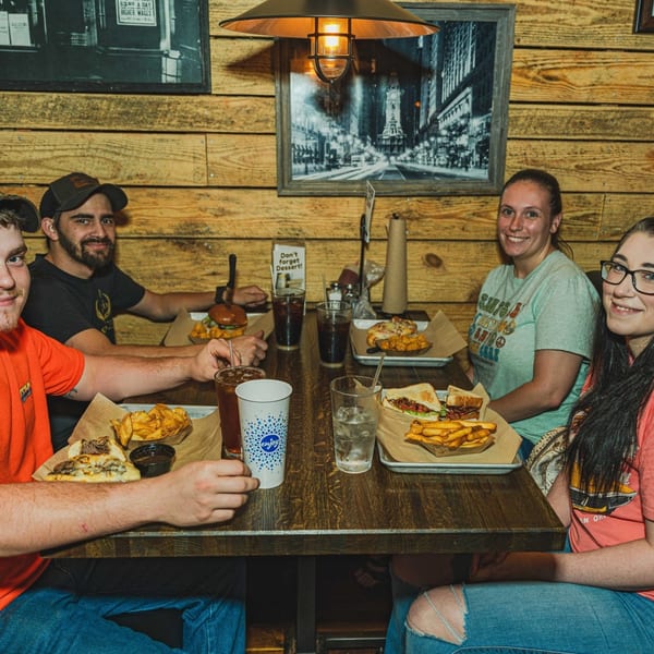 Four happy customers enjoying cheesesteaks and fries at Inky's Authentic Philadelphia Cheesesteaks and Hoagies.
