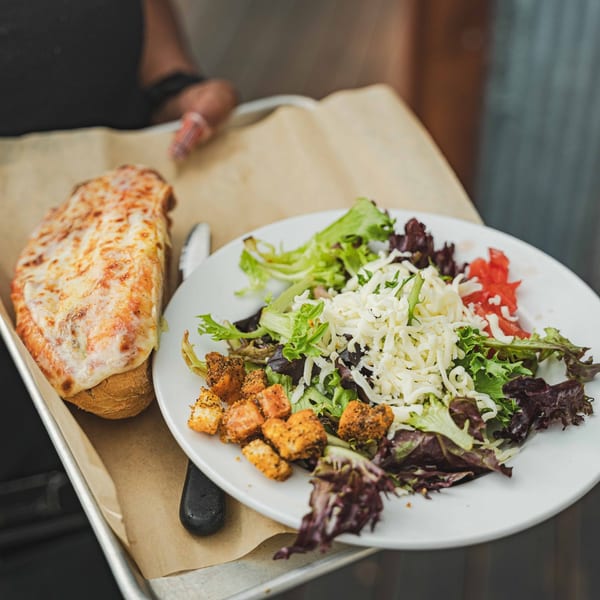 A tray with a cheesy hoagie and a side salad topped with shredded cheese and croutons.