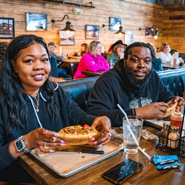 Two customers enjoying cheesesteaks at Inky's, with other diners in the background.
