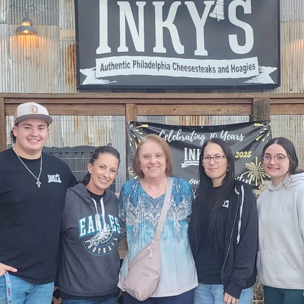 Five people smiling in front of the Inky's Authentic Philadelphia Cheesesteaks and Hoagies sign.
