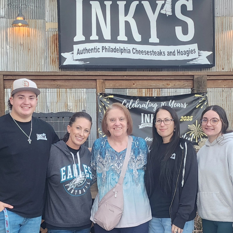 Five people smiling in front of the Inky's Authentic Philadelphia Cheesesteaks and Hoagies sign.