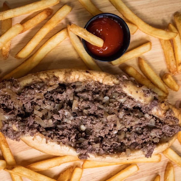 Inky's cheesesteak with melted cheese and onions, surrounded by golden french fries and ketchup.