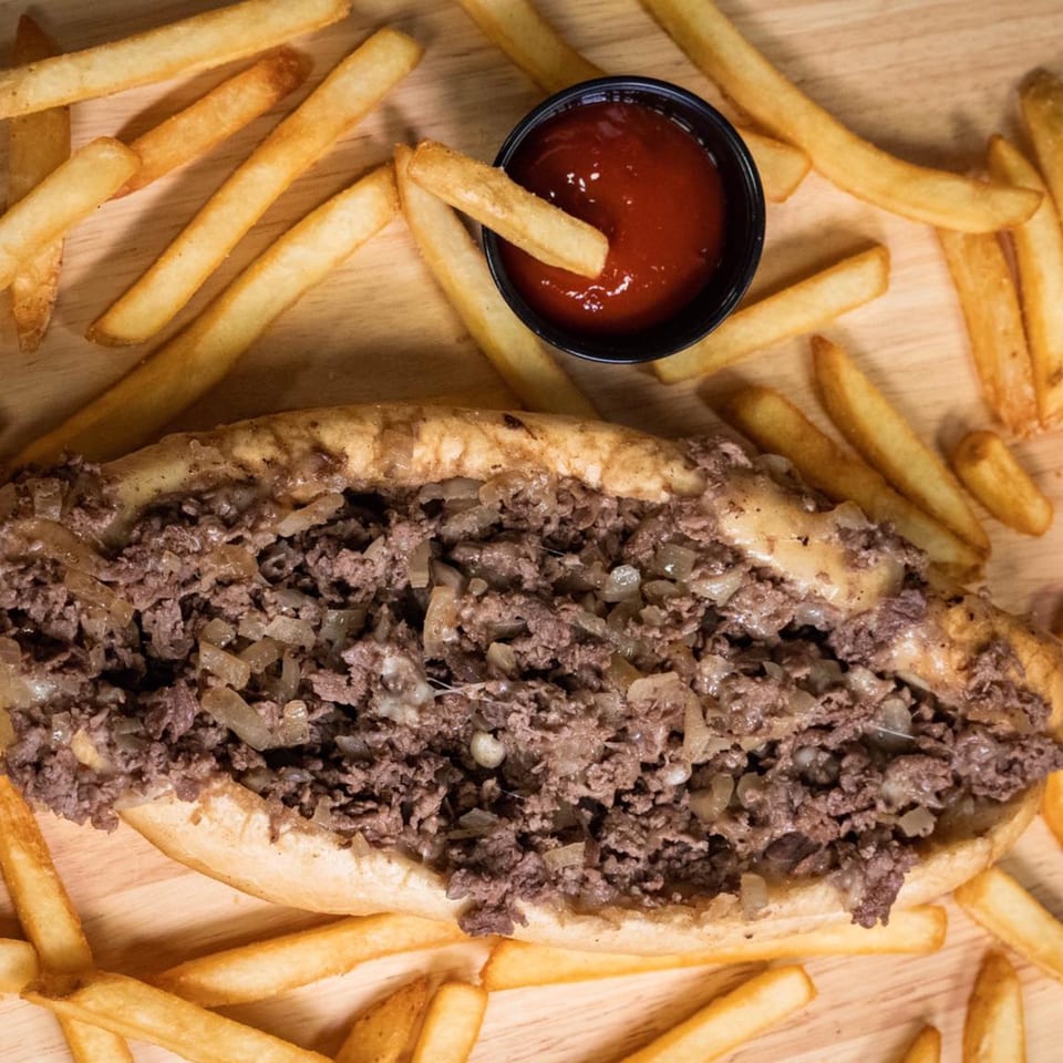 Inky's cheesesteak with melted cheese and onions, surrounded by golden french fries and ketchup.