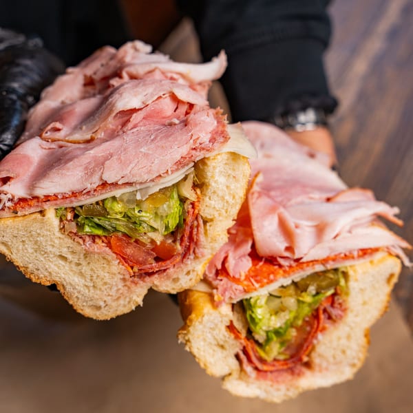 Two halves of a large Inky's hoagie, overflowing with deli meats, cheese, lettuce, and peppers.