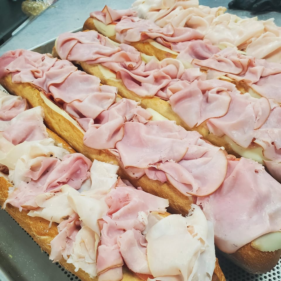 Rows of Inky's hoagies with ham and cheese on a metal tray.